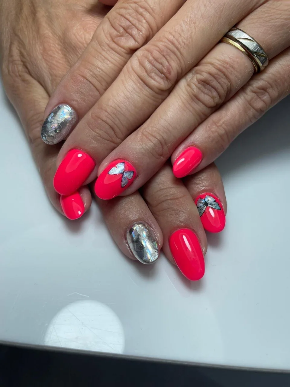 Manicura semipermanent coral neó amb papallones i efecte mirall plata